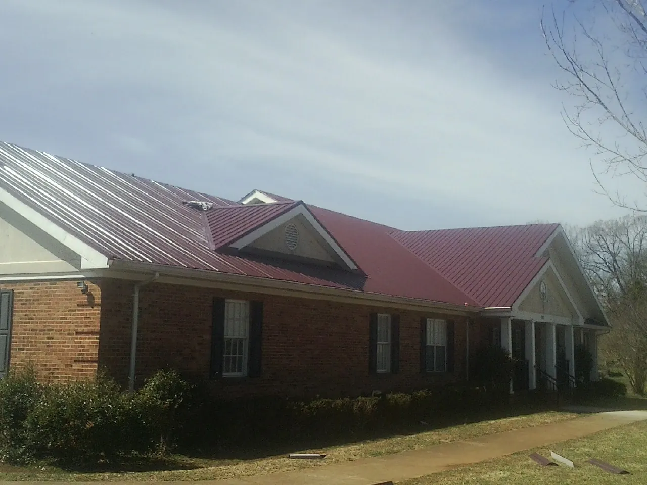 Red metal roof with gabled entries on a long brick building, from a Hail Damage Roof Repair job in Howe