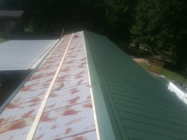 Old rusted panels beside newly installed green metal roofing — Wind Damage Roof Repair by Roofing Brothers in Howe