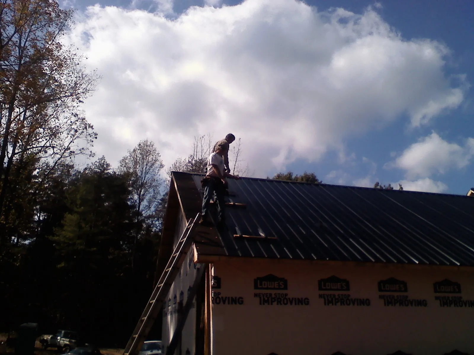 Roofer fastening dark metal panels high against a cloudy sky, from a Roof Inspection job in Howe